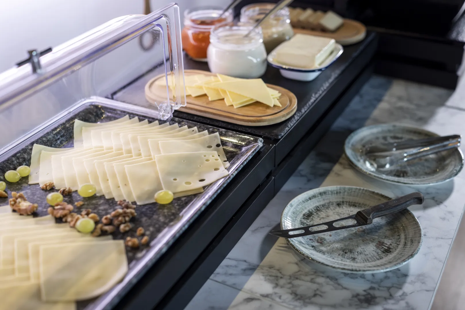 Breakfast buffet with cheese slices, grapes, and nuts on marble countertop.