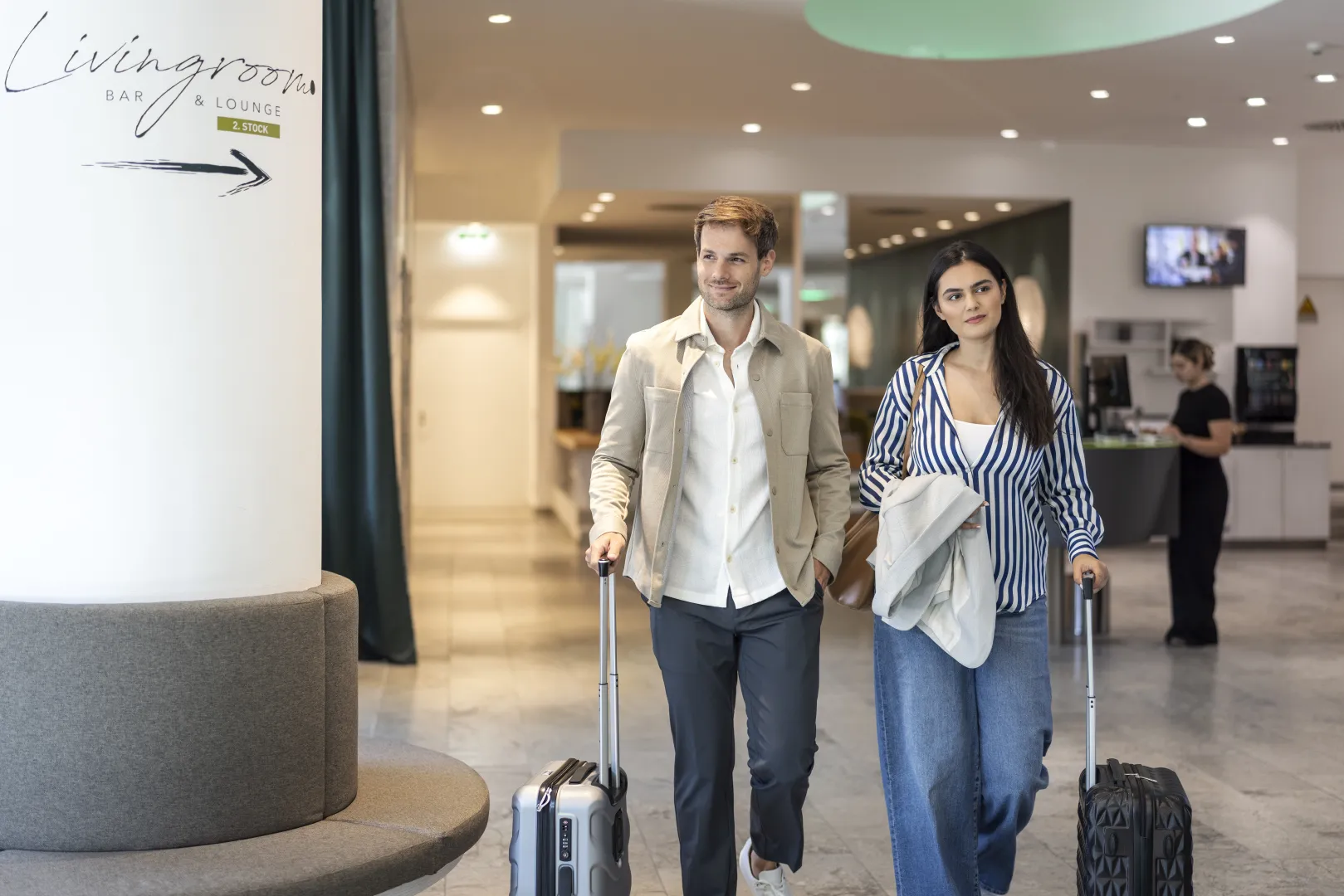 A couple with rolling suitcases entering a modern hotel, smiling and relaxed.