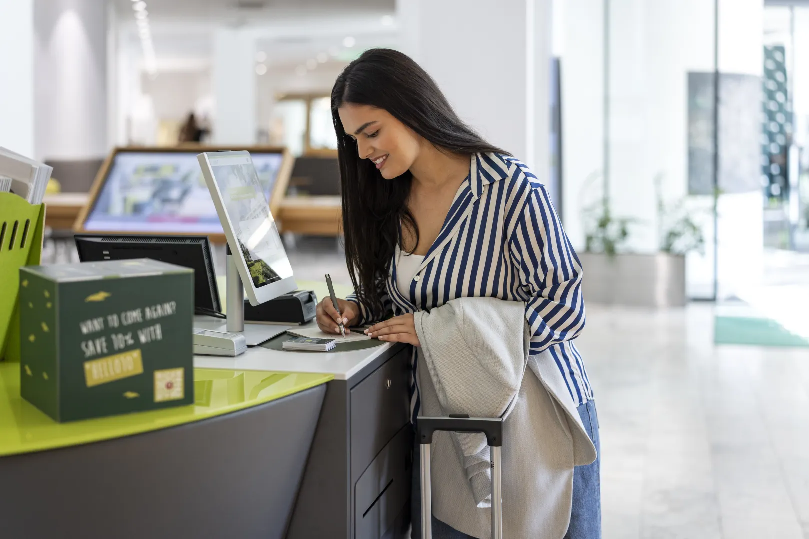 Woman at the hotel reception checking in at the counter with luggage.