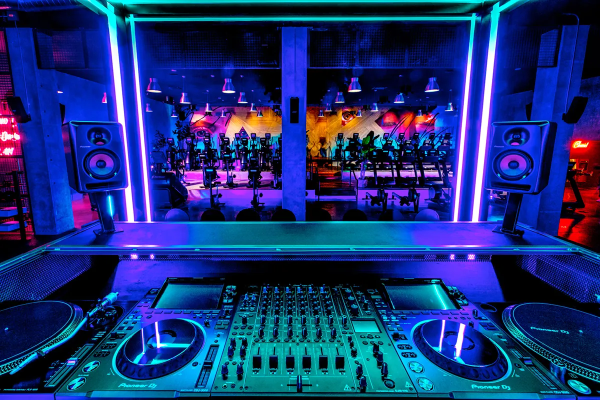 DJ booth overlooking a stylishly lit gym with workout equipment.
